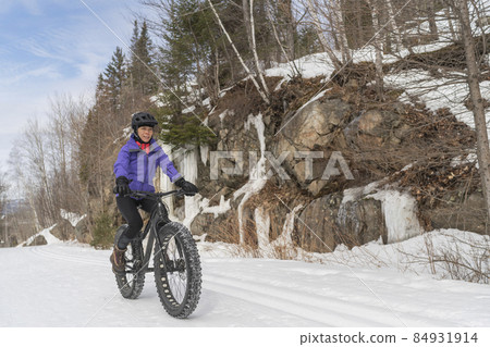 Fatbike in winter. Woman Fat biker riding fat bike bicycle in the snow in winter forest mountain landscape. Woman living healthy outdoor active lifestyle 84931914