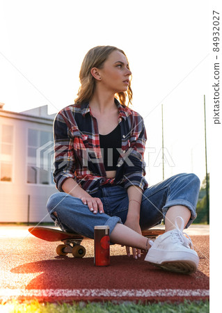 Young millennial woman hippie sitting on skateboard. Summer Skate Sessions. Woman cruising on a longboard in a park. Carefree female skater 20s enjoying freedom youth lifestyle Young millennial woman hippie sitting on skateboard. Summer Skate Sessions. Woman cruising on a longboard in a park. Carefree female skater 20s enjoying freedom youth lifestyle 84932027