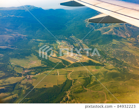View of airplane wing, blue skies and green land during landing. Airplane window view. 84932223