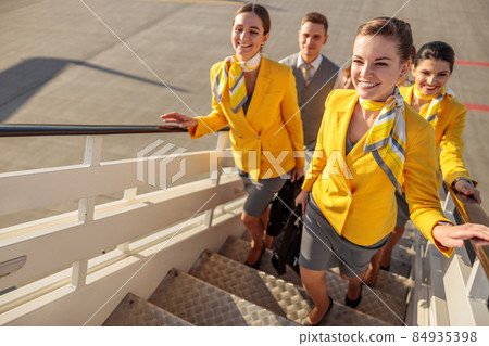 Smiling airline workers walking up airplane stairs 84935398