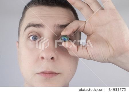 Conceptual shot of an eye crystalline lens replacement. Ophthalmic surgery. Return of sight. Removal of cataracts. Surgical intervention in the eyeball. Doctor holds the implant near the patient 84935775