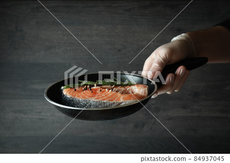 Male hand in glove hold pan with salmon meat, close up Male hand in glove hold pan with salmon meat, close up 84937045