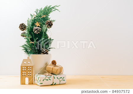Creative natural miniature Christmas tree in pot on wooden table with gift boxes and white background. Xmas greeting card with copy space. Happy New Year. Creative natural miniature Christmas tree in pot on wooden table with gift boxes and white background. Xmas greeting card with copy space. Happy New Year. 84937572