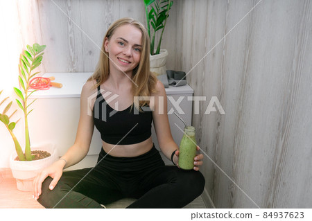 Young millenial blond woman drinking vegan smoothie drink detox. Woman doing yoga exercises at home. Clean eating, weight loss, healthy dieting food concept. Stay healthy 84937623