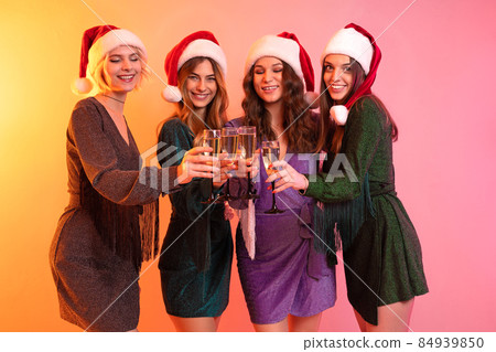 Happy Santa girls in festive dresses celebrates New Year while holding glasses of champagne 84939850