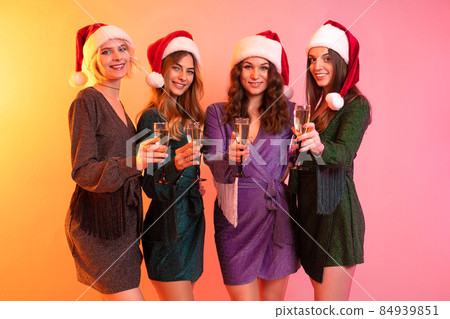Four happy girls in Santa Claus hats holds glasses of champagne having fun. New Year party Four happy girls in Santa Claus hats holds glasses of champagne having fun. New Year party 84939851