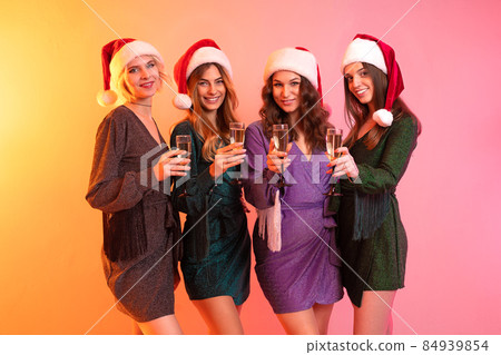 Cheerful Santa girls in festive dresses celebrates New Year while holding glasses of champagne Cheerful Santa girls in festive dresses celebrates New Year while holding glasses of champagne 84939854