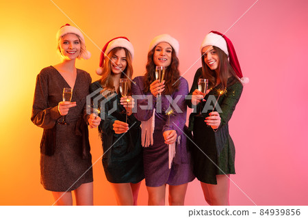 Beautiful Santa girls in festive dresses celebrates New Year while holding glasses of champagne 84939856