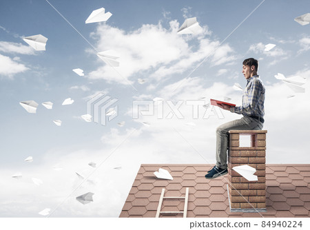 Handsome student guy reading book and paper planes flying in air Handsome student guy reading book and paper planes flying in air 84940224
