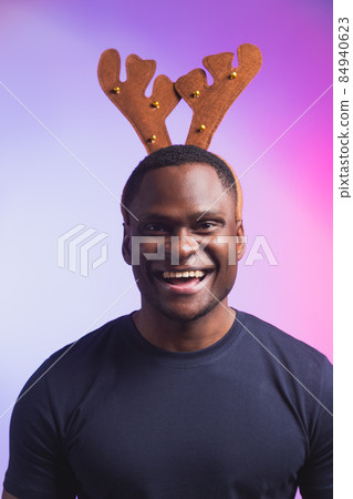 Portrait of african american man wears rudolph deer horns enjoy his accessory for christmas eve party celebration on colourful background Portrait of african american man wears rudolph deer horns enjoy his accessory for christmas eve party celebration on colourful background 84940623