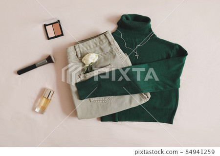 Overhead view of woman's casual outfit. Beige jeans, green knitted sweater, cosmetics and accessories lie on beige background. Trendy stylish women clothes. Flat lay, top view Overhead view of woman's casual outfit. Beige jeans, green knitted sweater, cosmetics and accessories lie on beige background. Trendy stylish women clothes. Flat lay, top view 84941259