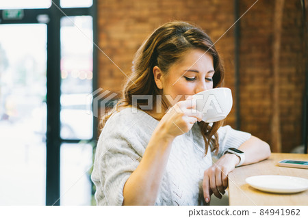 Young Woman drinking coffee or tea during the break or lunch time in the cafe. Time to relax Young Woman drinking coffee or tea during the break or lunch time in the cafe. Time to relax 84941962