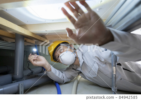 A man in work clothes inspecting the underfloor of a house A man in work clothes inspecting the underfloor of a house 84942585
