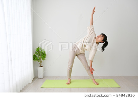 Young woman doing stretching exercises on an indoor mat Young woman doing stretching exercises on an indoor mat 84942930