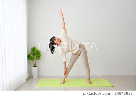 Young woman doing stretching exercises on an indoor mat Young woman doing stretching exercises on an indoor mat 84942932