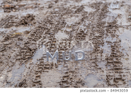 the word mud composed of silver metal letters on wet dirt surface 84943059