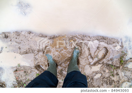 feet in green rubber boots stands in wet brown mud puddle directly above view feet in green rubber boots stands in wet brown mud puddle directly above view 84943093