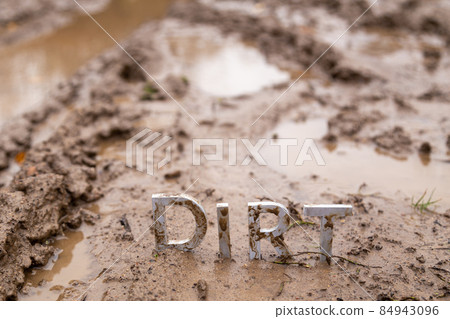 the word dirt composed of silver metal letters on wet clay surface 84943096