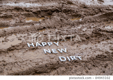 the words happy new dirt laid with silver metal letters on wet mud surface 84943102