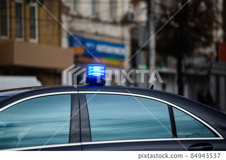 blue flashing light on top of black government car on daytime city street blue flashing light on top of black government car on daytime city street 84943537