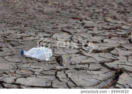 empty crumpled plastic bottle on dry cracked mud desert like gray background 84943632