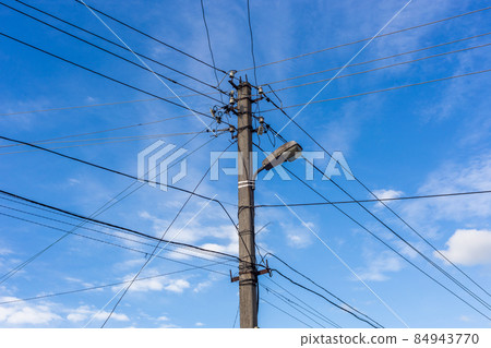 Concrete lamp post with many cables connected radially on blue sky with feather clouds in the background, Centered composition. Concrete lamp post with many cables connected radially on blue sky with feather clouds in the background, Centered composition. 84943770