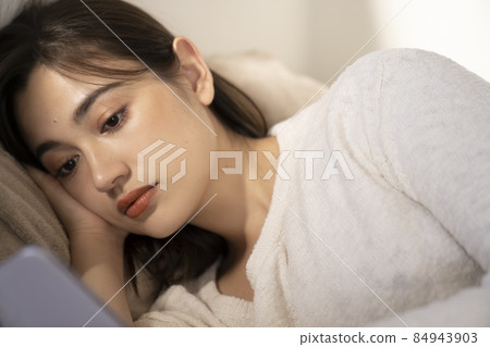 一名婦女在床上的看一個智能手機 一名婦女在床上的看一個智能手機 84943903
