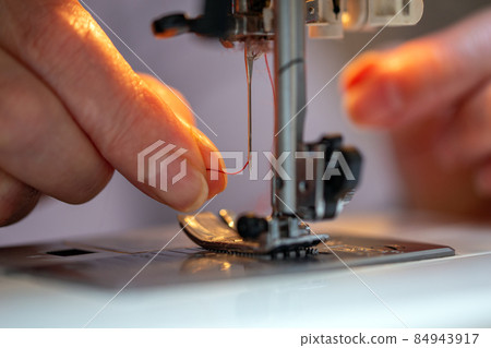 grandma fingers inserting a red thread into a sewing machine's needle, close-up 84943917