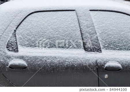 black car covered with snow at cloudy day light - close-up side view 84944100