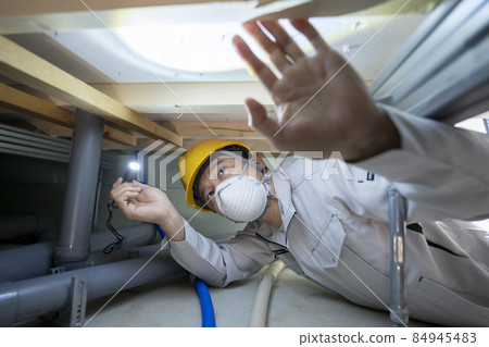 A man in work clothes inspecting the underfloor of a house 84945483