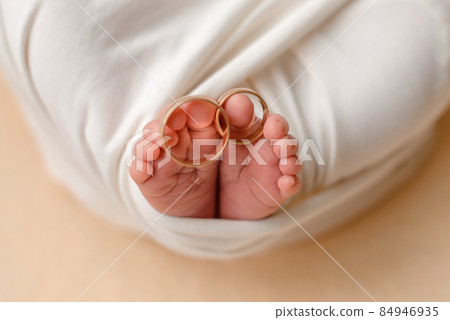 Little feet of a newborn baby with his parents' wedding rings on his fingers 84946935