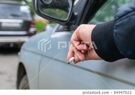 The driver holds a cigarette in his hand sticking it out of the window The driver holds a cigarette in his hand sticking it out of the window 84947022