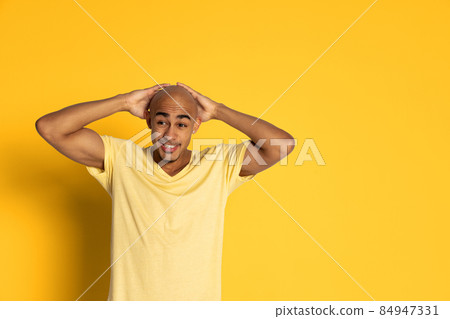 Emotional dark skinned man in t-shirt posing isolated on yellow color studio background. Concept of human emotions 84947331