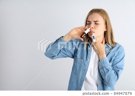 Woman with nasal drops and thermometer on light background, runny nose concept 84947879
