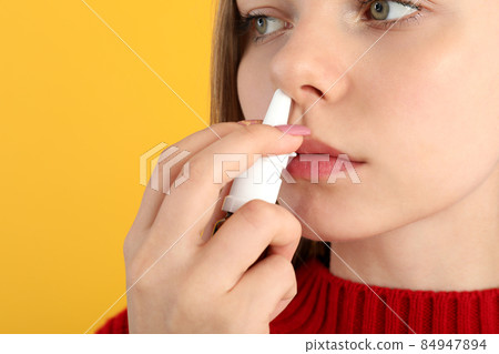 Young woman with nasal drops on yellow background, runny nose concept 84947894