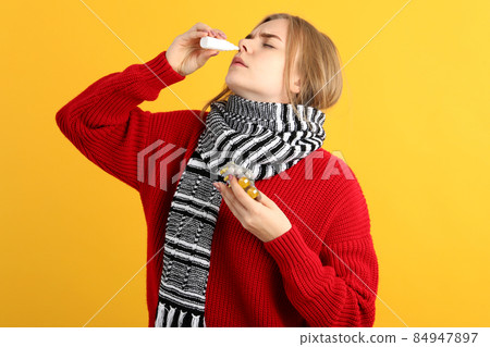 Young woman with nasal drops on yellow background, runny nose concept 84947897