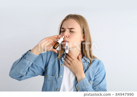 Woman with nasal drops and thermometer on light background, runny nose concept 84947990