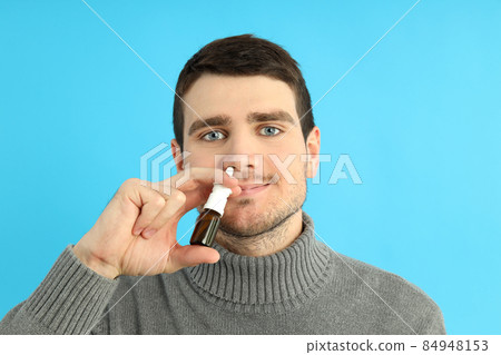 Young man with nasal spray on blue background, runny nose concept 84948153