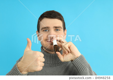 Young man with nasal spray on blue background, runny nose concept 84948258