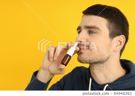 Young man with nasal spray on yellow background, runny nose concept 84948262