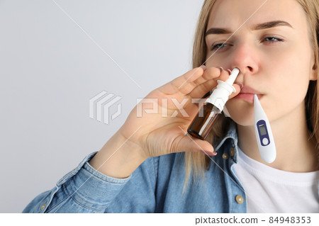 Woman with nasal drops and thermometer on light background, runny nose concept 84948353