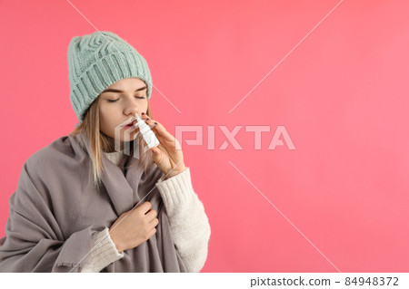 Young woman using nasal spray on pink background, runny nose concept 84948372