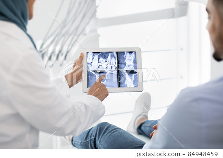 Oral Surgery. Female Dentist In Hijab Demonstrating Teeth Xray On Digital Tablet Oral Surgery. Female Dentist In Hijab Demonstrating Teeth Xray On Digital Tablet 84948459