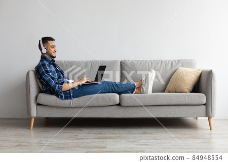 Smiling Arab man in headphones using pc at home Smiling Arab man in headphones using pc at home 84948554