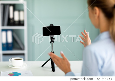 Young business blogger recording video on cellphone, talking to mobile phone with blank screen on tripod Young business blogger recording video on cellphone, talking to mobile phone with blank screen on tripod 84948735