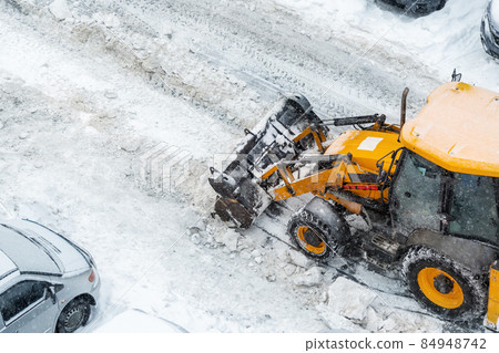 Tractor loader machine uploading dirty snow into dump truck. Cleaning city street, removing snow and ice after heavy snowfalls and blizzard. Snowplow outdoors clean pavement sidewalk road driveway Tractor loader machine uploading dirty snow into dump truck. Cleaning city street, removing snow and ice after heavy snowfalls and blizzard. Snowplow outdoors clean pavement sidewalk road driveway 84948742