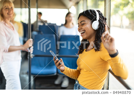 Excited black lady dancing in city bus wearing headphones Excited black lady dancing in city bus wearing headphones 84948870