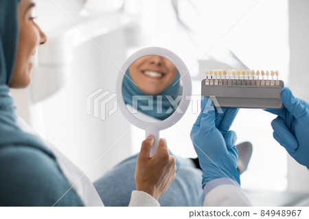 Restorative Dentistry. Muslim Female Patient Holding Mirror And Looking At Her Smile 84948967