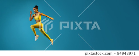 Athletic Female Jumping Running In Mid-Air Looking Aside, Blue Background 84948971