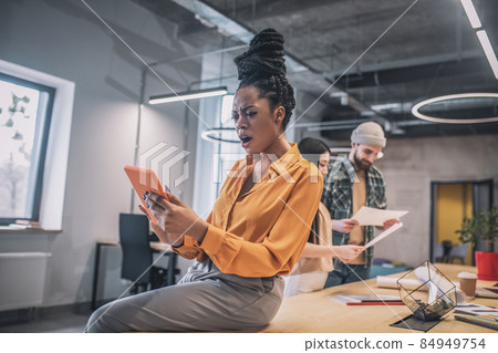 Dark-skinned surprised girl looking at tablet Dark-skinned surprised girl looking at tablet 84949754